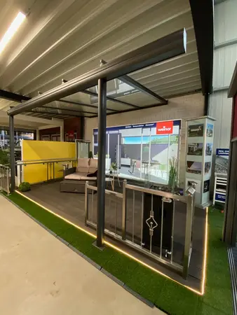 Überdachte Terrasse mit Lounge-Möbeln, Geländer und Kunstrasen in moderner Ausstellung.