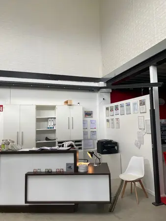 Modernes Büro mit Empfangstresen, weißen Möbeln, Drucker und Zertifikaten an der Wand.