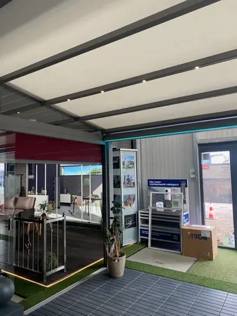 Überdachte Terrasse mit moderner Markise, Gartenmöbeln und Ausstellungsbereich für Bauelemente.
