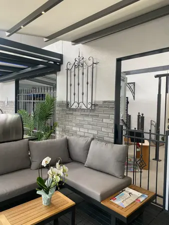 Moderne Terrasse mit grauem Sofa, Couchtisch, Orchidee und stilvollem Metallzaun.