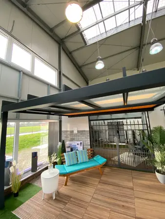 Moderner Ausstellungsraum mit überdachter Terrasse, Gartenmöbeln und Pflanzen.