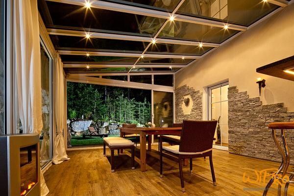 Moderner Wintergarten mit Glasdach, stilvoller Beleuchtung und Blick auf Garten.