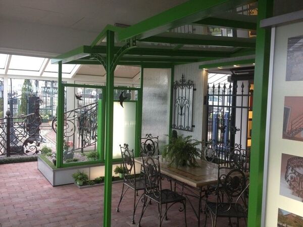 Überdachte Terrasse mit schmiedeeisernen Gartenmöbeln und grünem Metallpavillon.