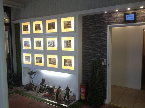 Beleuchtete Immobilien-Exposés und Skulpturen im modernen Eingangsbereich eines Maklerbüros.